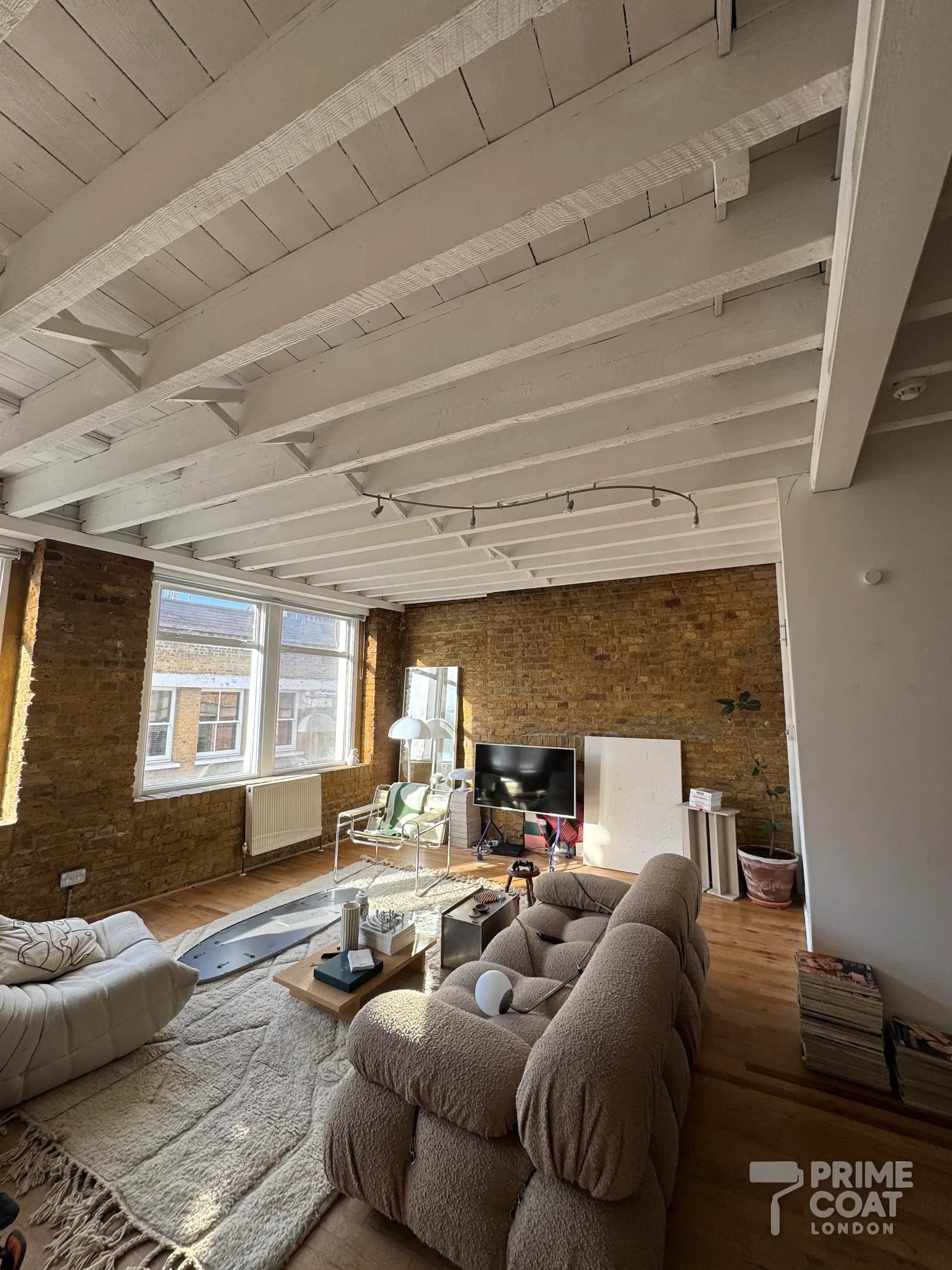Shoreditch E2 warehouse flat after painting — timber joists, boards and main beam painted white with the brick walls left exposed