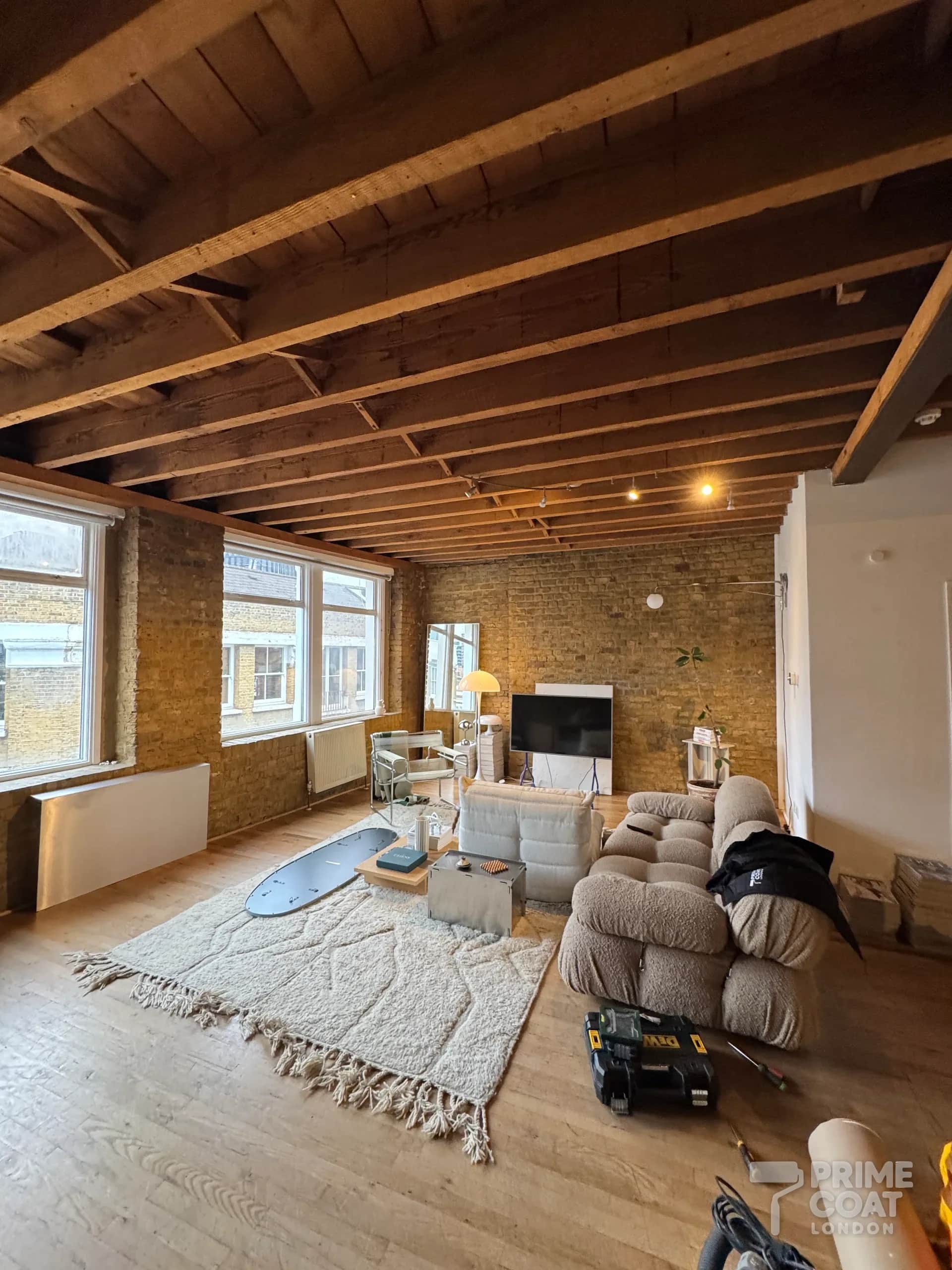 Shoreditch E2 warehouse flat before painting — bare pine ceiling joists and boards above exposed London-stock brick walls