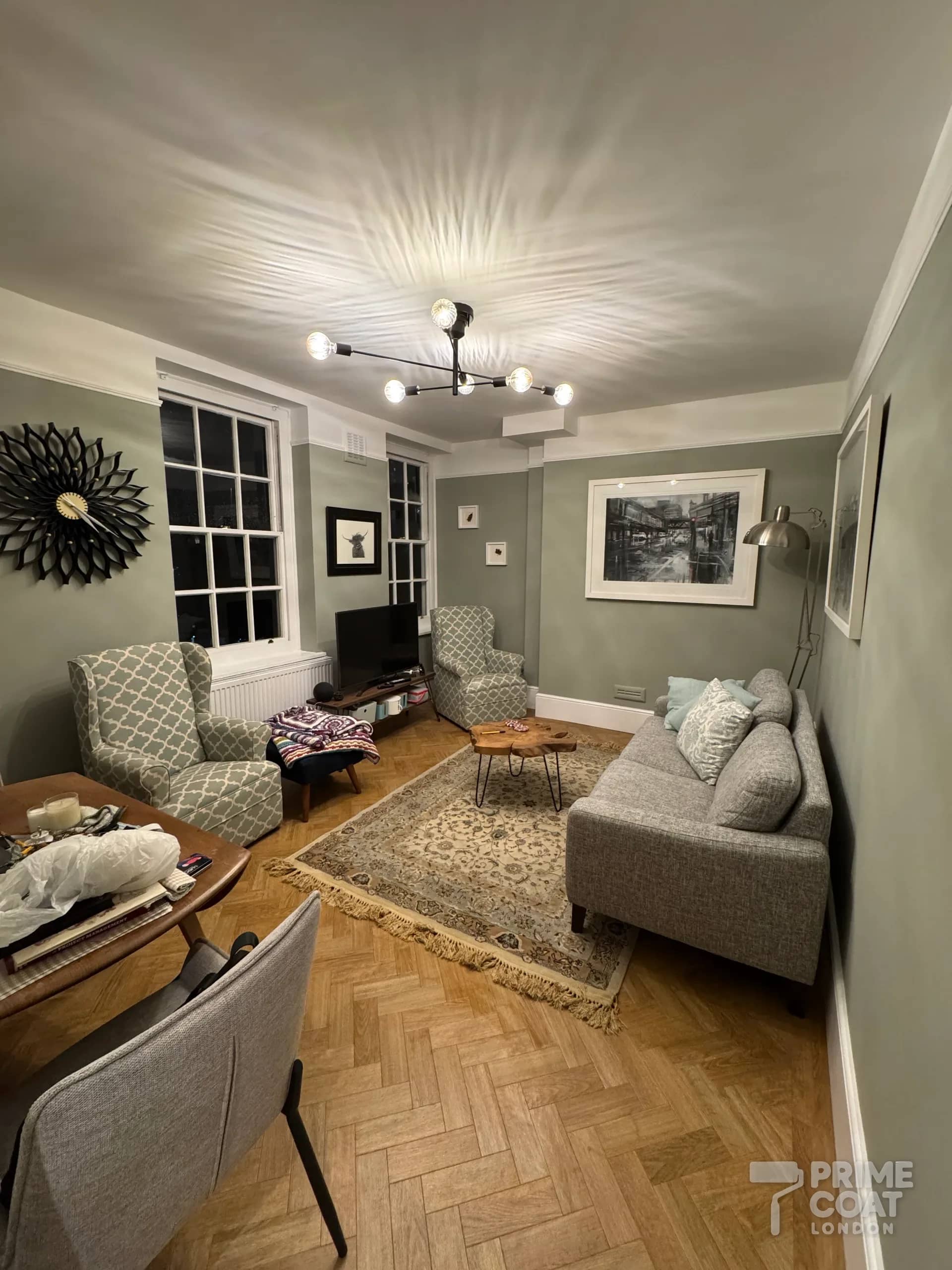 Finished living room of a Battersea SW11 period flat — green-grey walls, white cornice and sash windows above a parquet floor