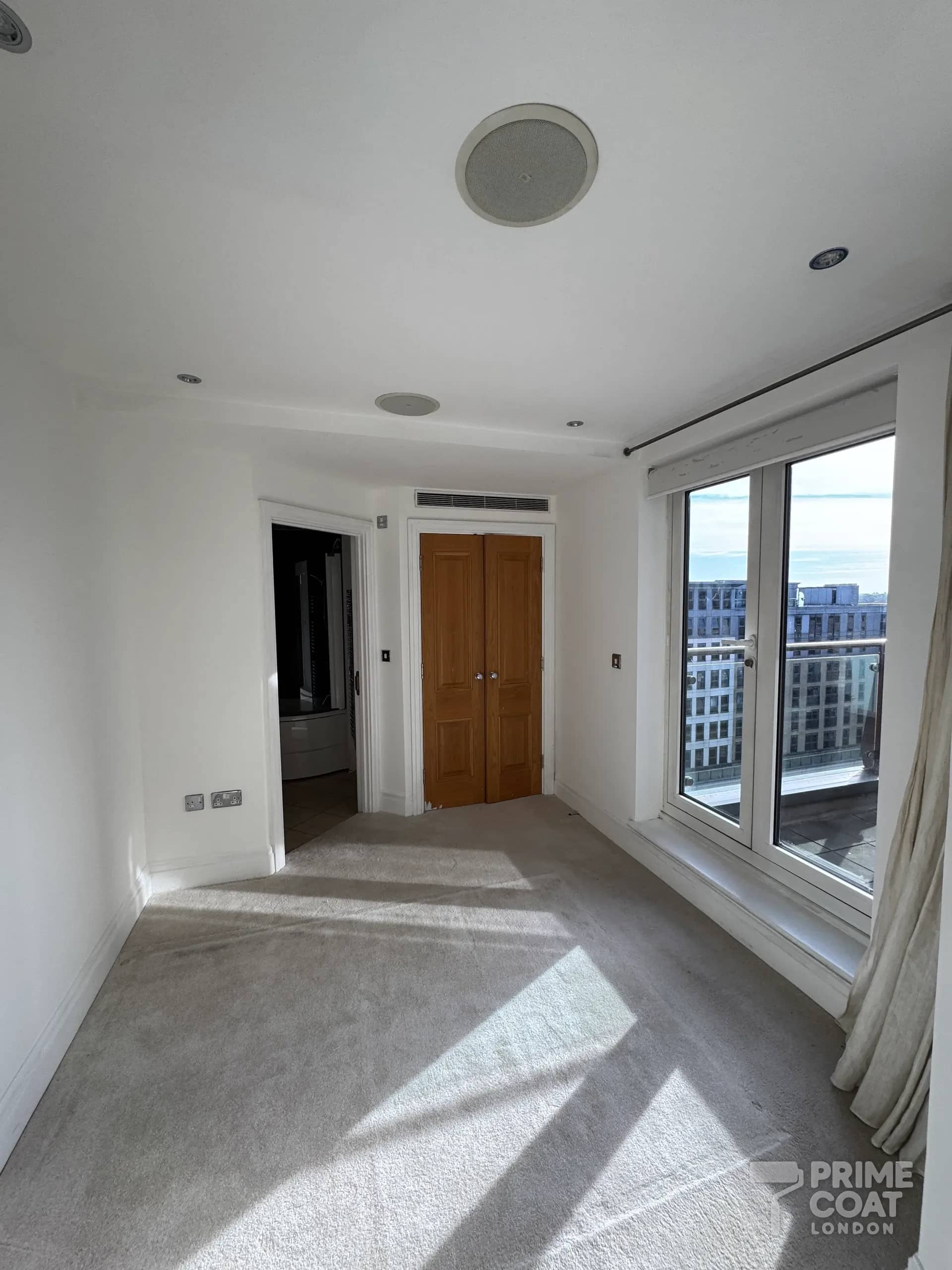 Second bedroom of a Chelsea Harbour SW10 apartment after painting — fresh white walls beside the balcony doors overlooking the marina