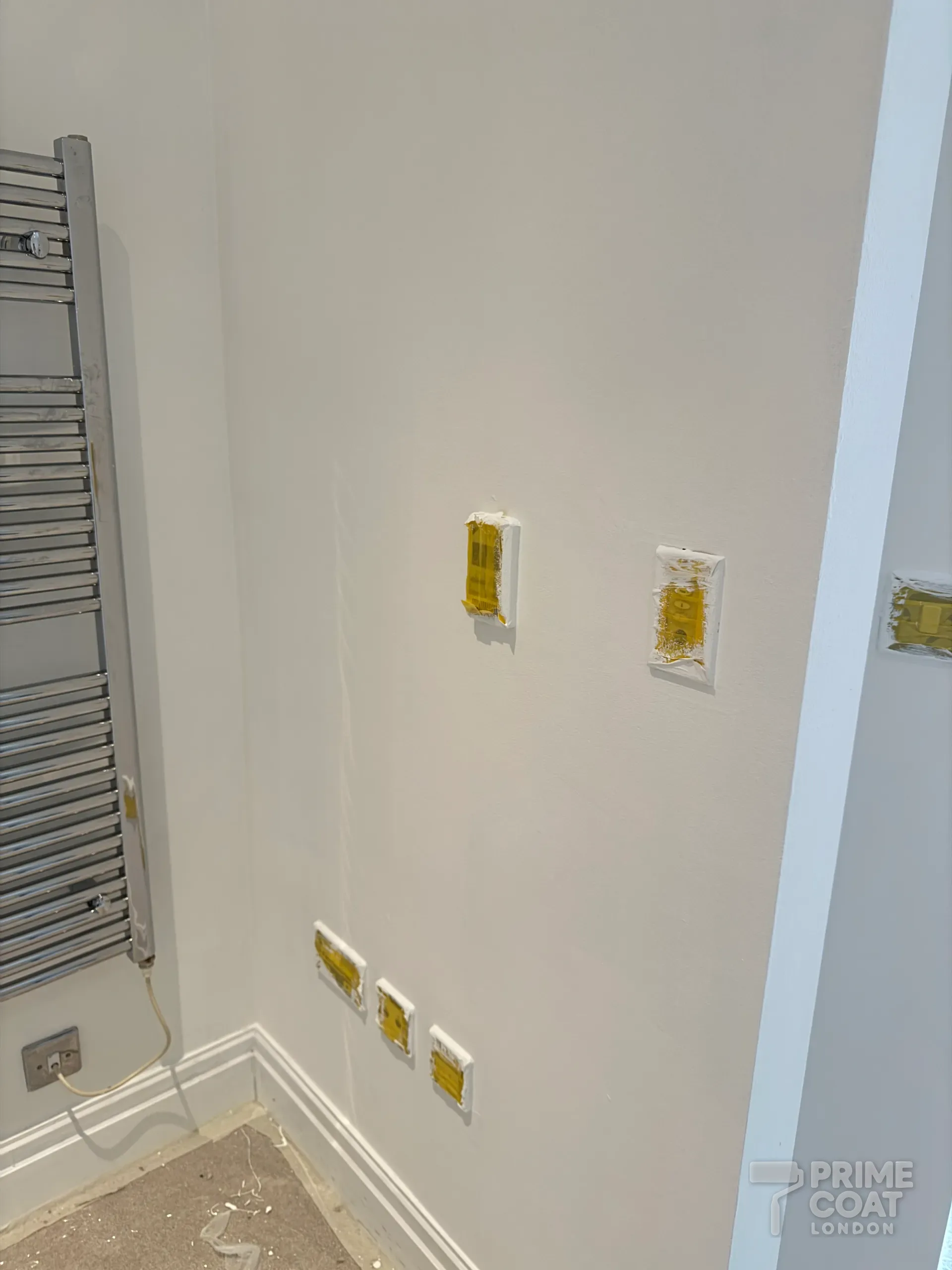 Freshly painted white wall in a Chelsea Harbour SW10 apartment with sockets and switches masked with tape during the work