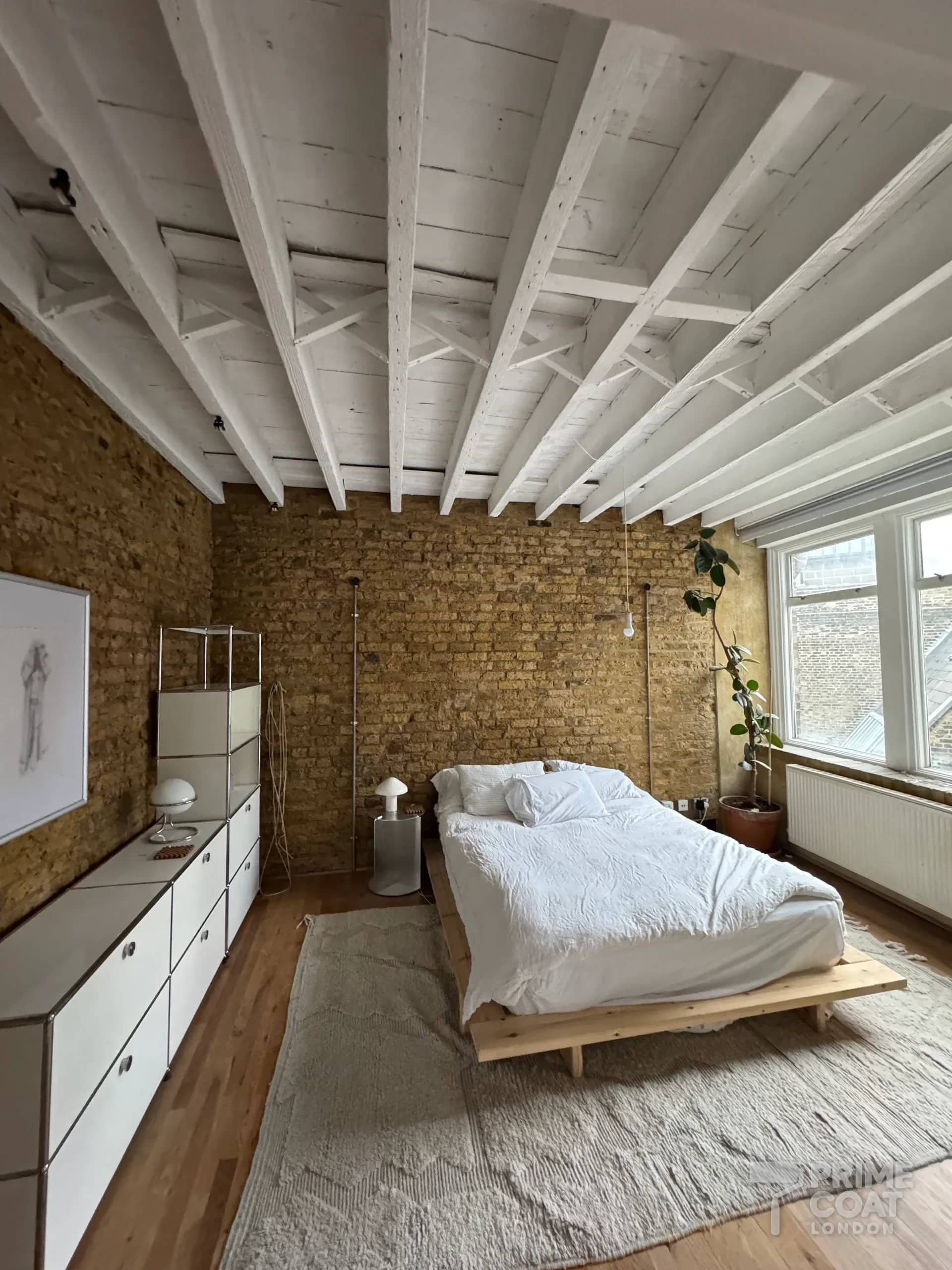 Finished bedroom in a Shoreditch E2 warehouse loft — white-painted timber ceiling above exposed yellow brick walls