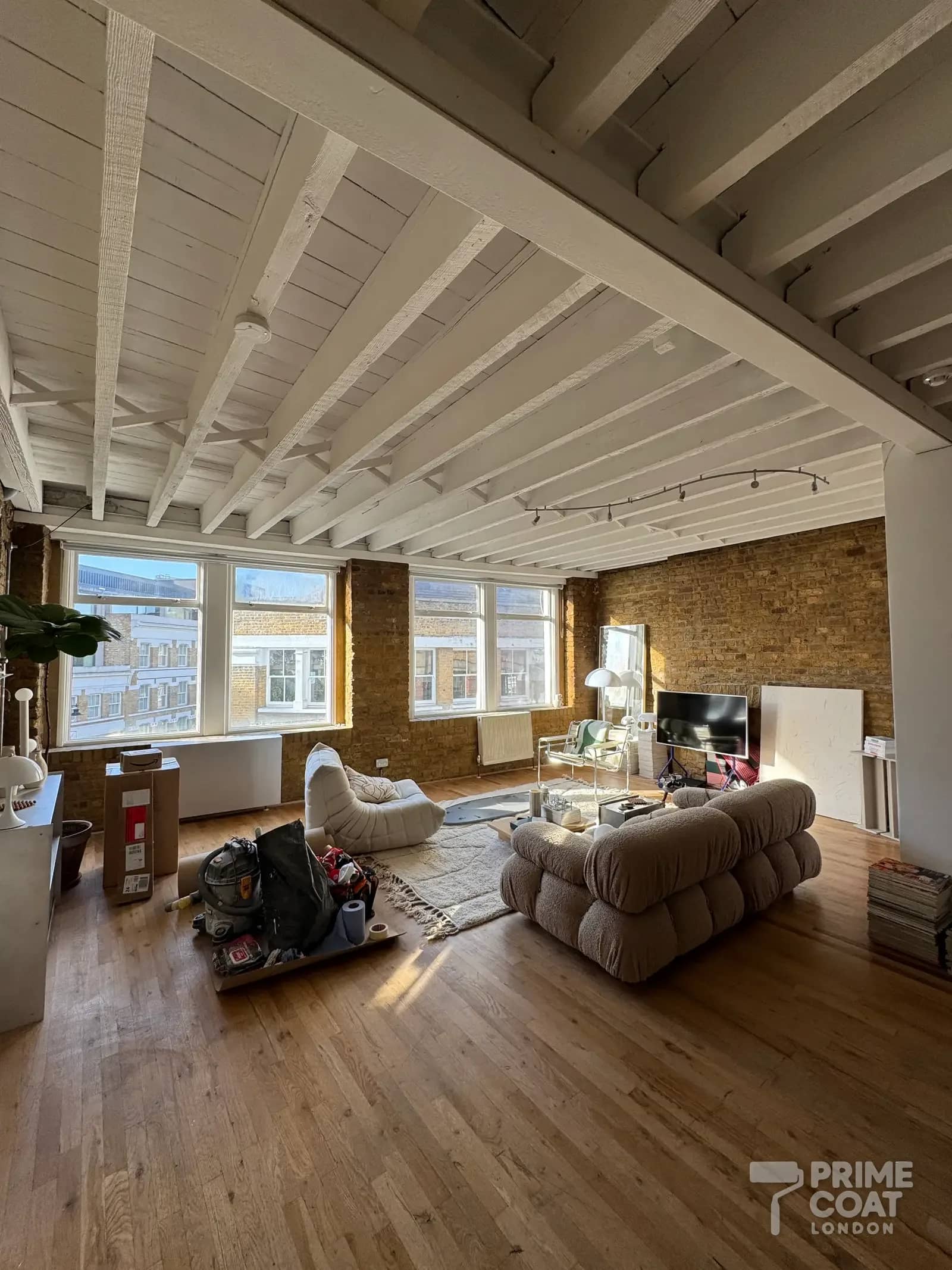Finished open-plan living room in a Shoreditch E2 loft — white timber ceiling and beams over brick walls and large warehouse windows