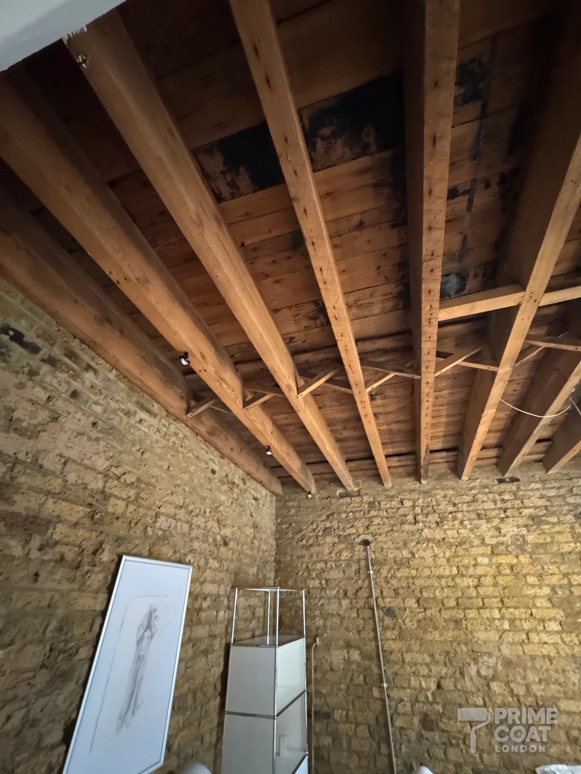 Timber ceiling in a Shoreditch E2 warehouse loft before painting — old joists and boards with dark water and soot staining