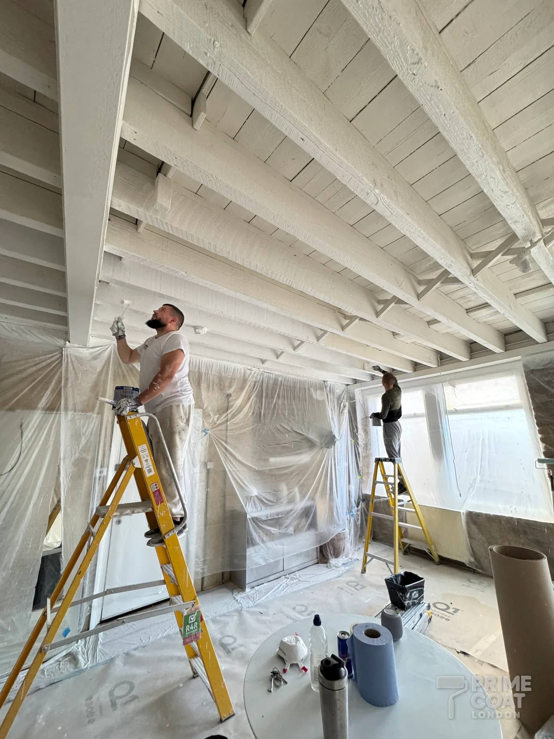 Two Prime Coat decorators on ladders painting the white timber ceiling of a Shoreditch E2 warehouse loft