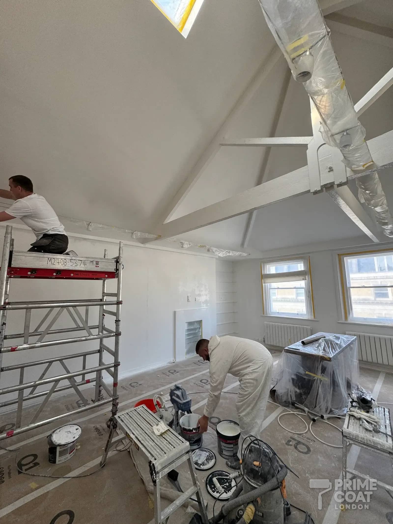 Prime Coat decorators spray-painting the vaulted ceiling and walls of a Kensington W8 reception with an airless sprayer, windows and lighting masked