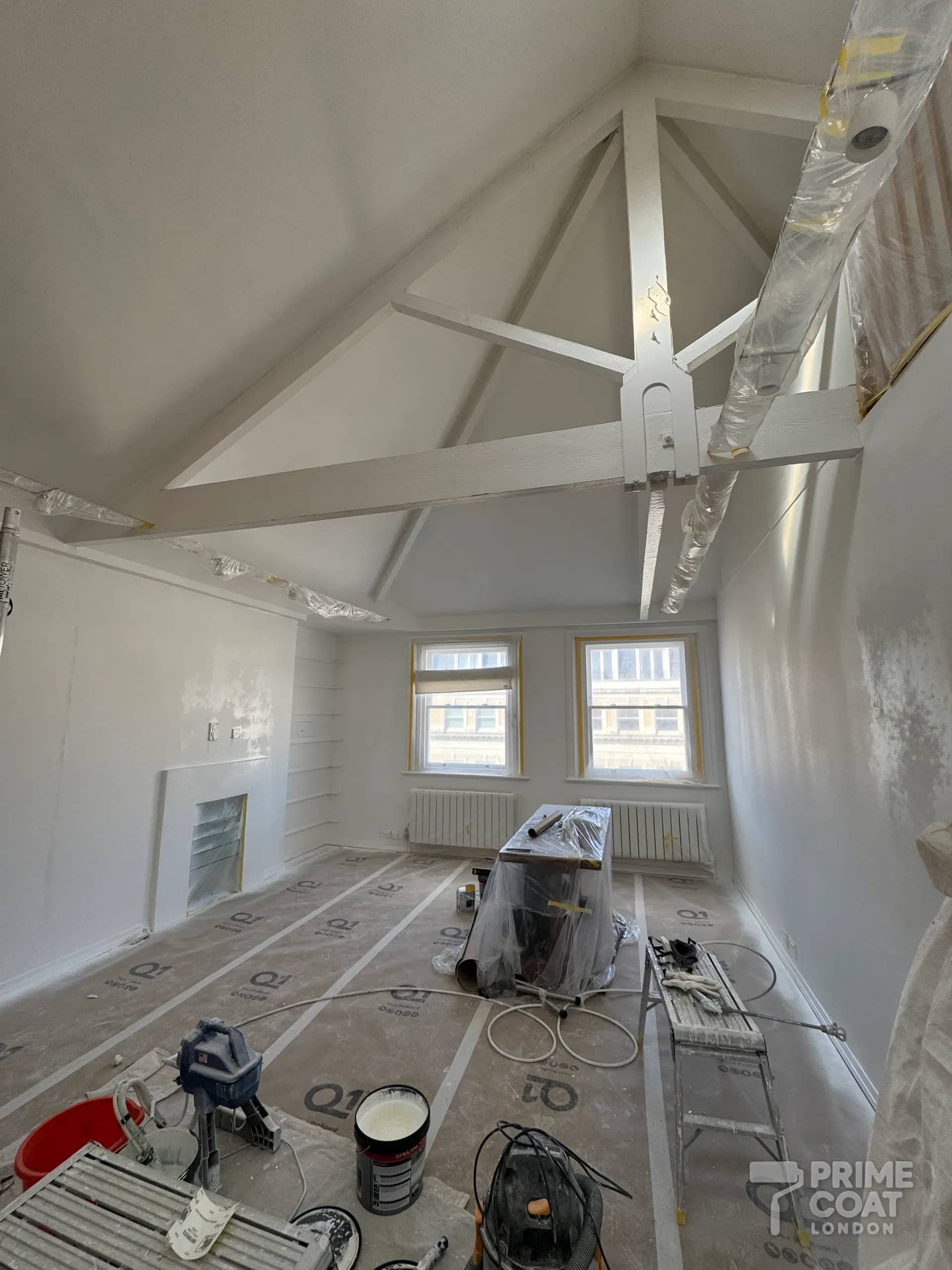 Exposed roof beams and high ceiling freshly sprayed white in a Kensington W8 flat, with the light track wrapped and sash windows masked