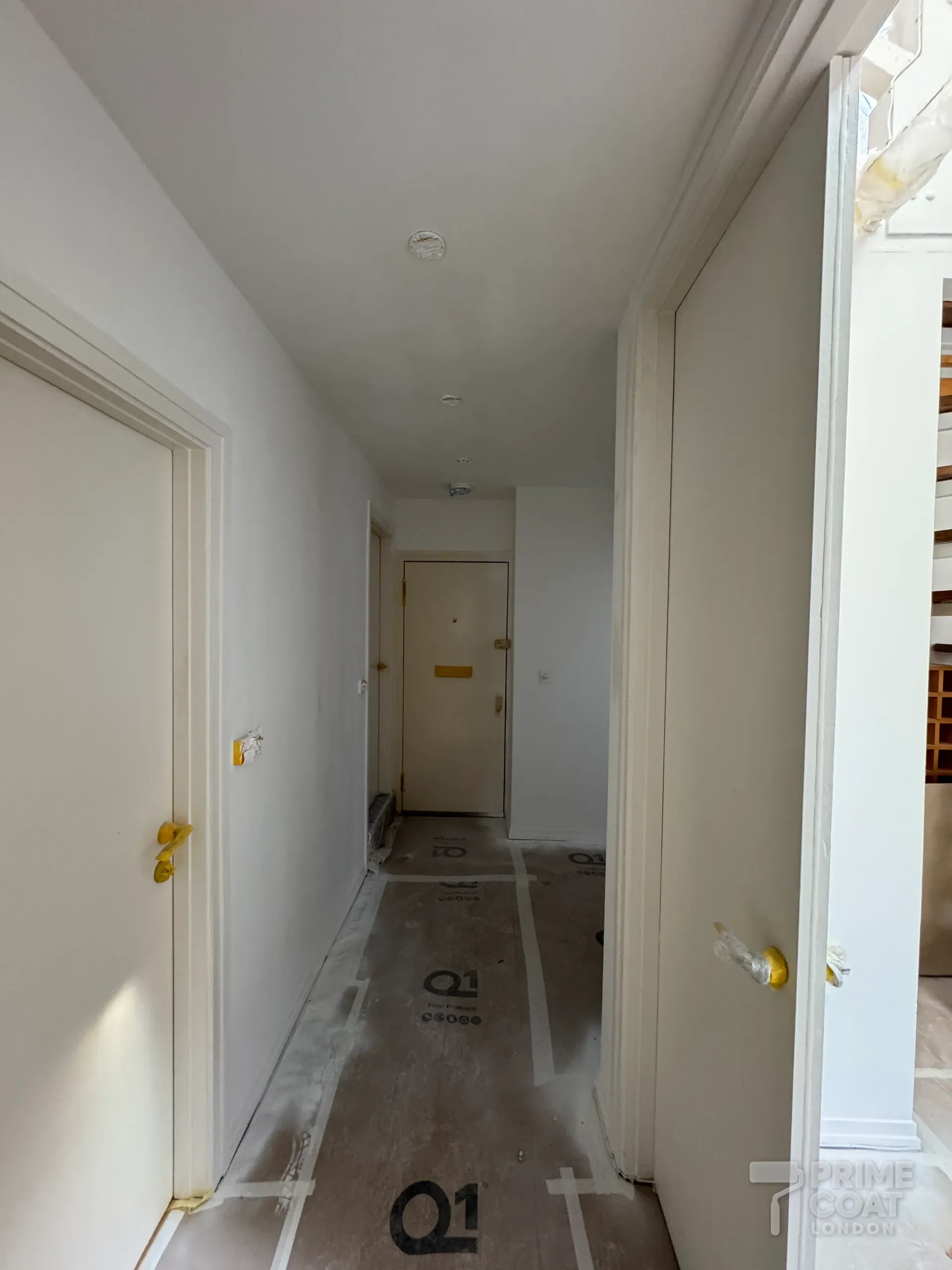 Hallway of a Kensington W8 flat with doors, door frames and walls sprayed white, handles taped and Q1 boards protecting the floor