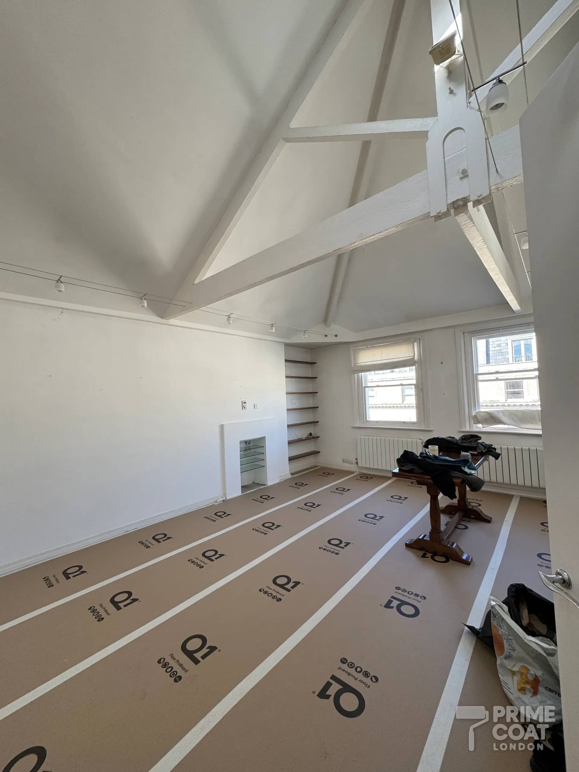 Vaulted reception in a Kensington W8 flat before spraying — Q1 Floor ProBoard taped across the whole floor beneath the exposed roof beams