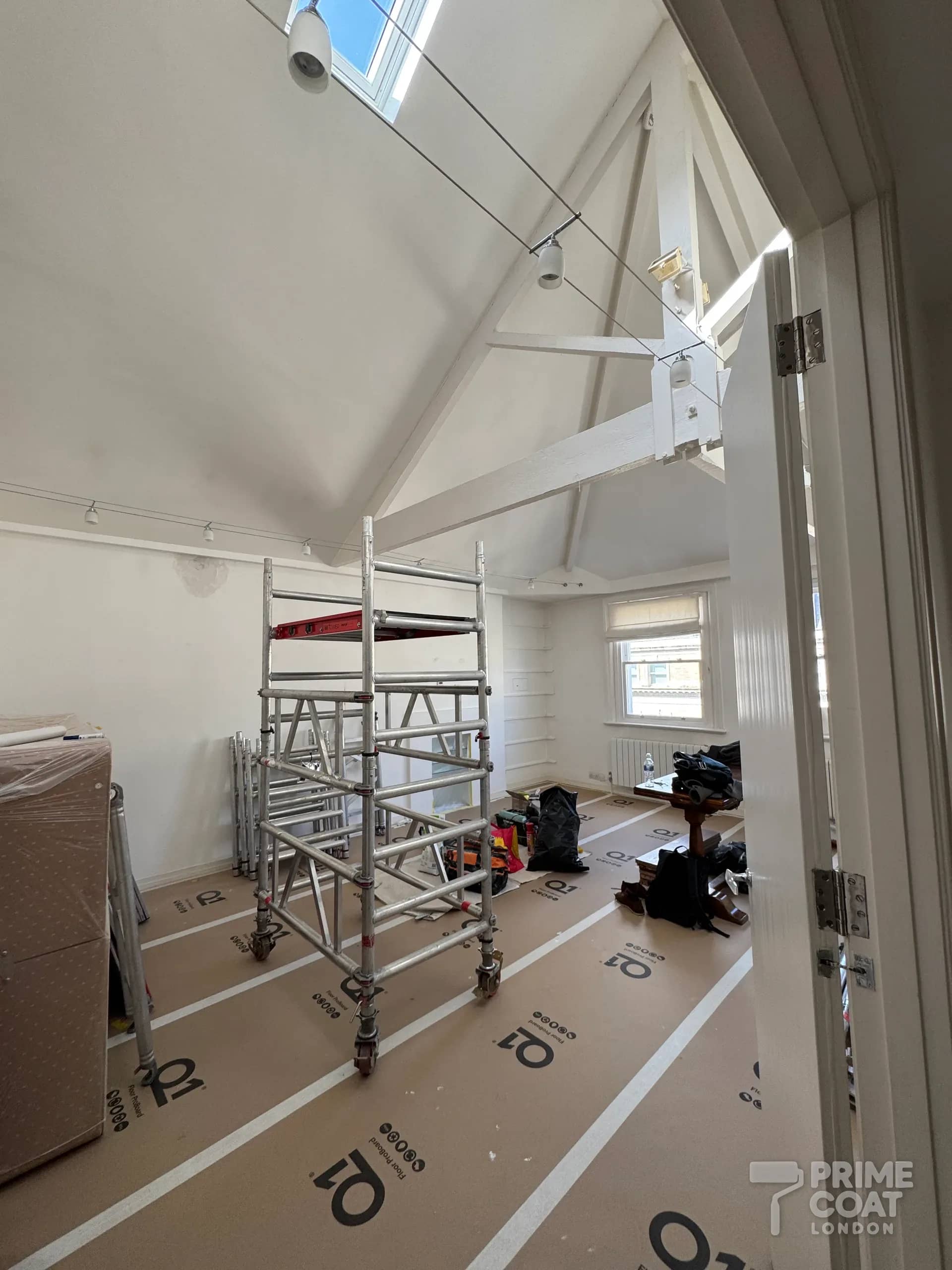 Mobile scaffold tower set up under the high vaulted ceiling and roof trusses of a Kensington W8 top-floor flat
