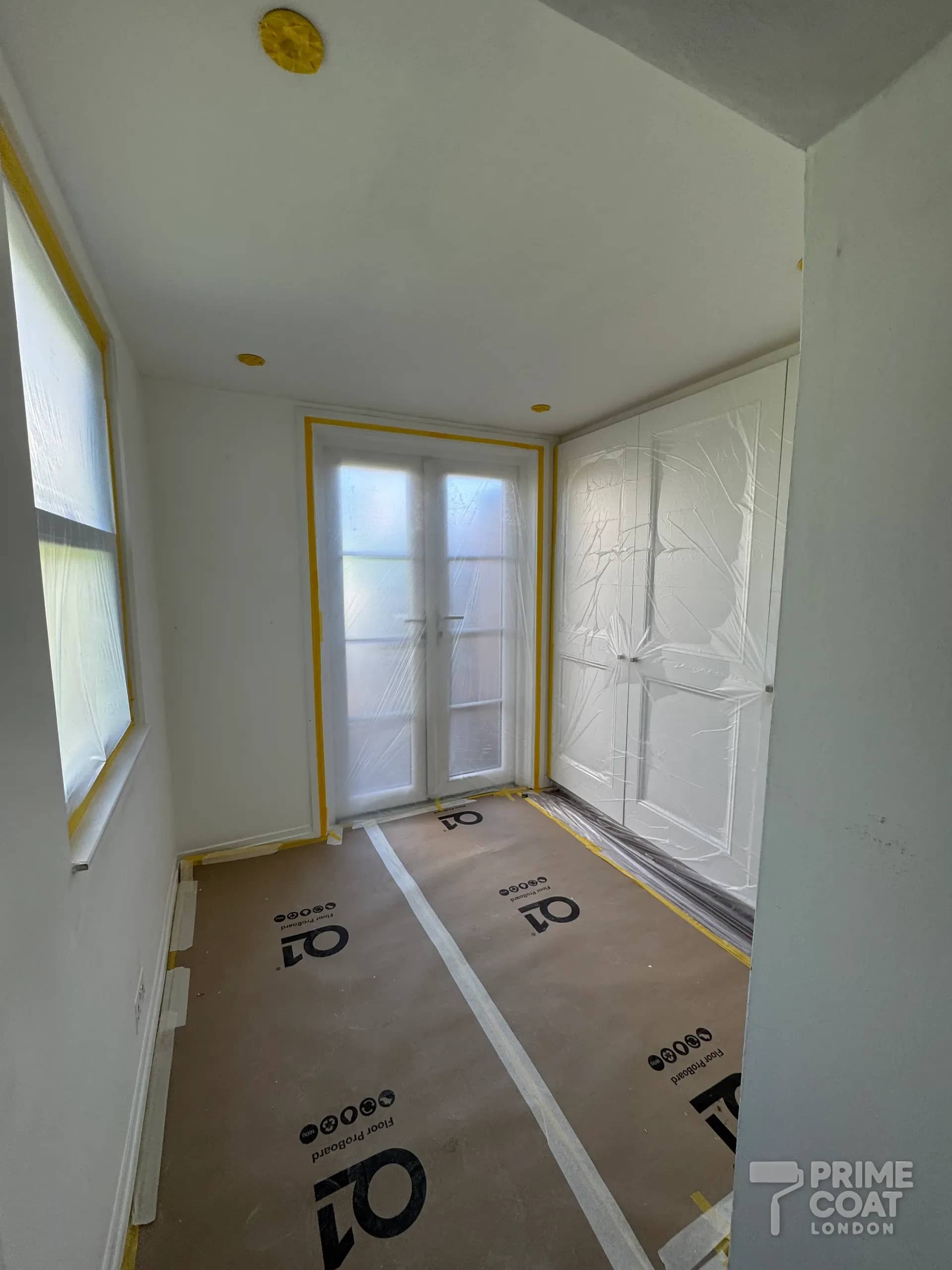 Room in a Kensington W8 flat with glazed doors and fitted wardrobes masked in plastic and tape, floor protected with Q1 boards
