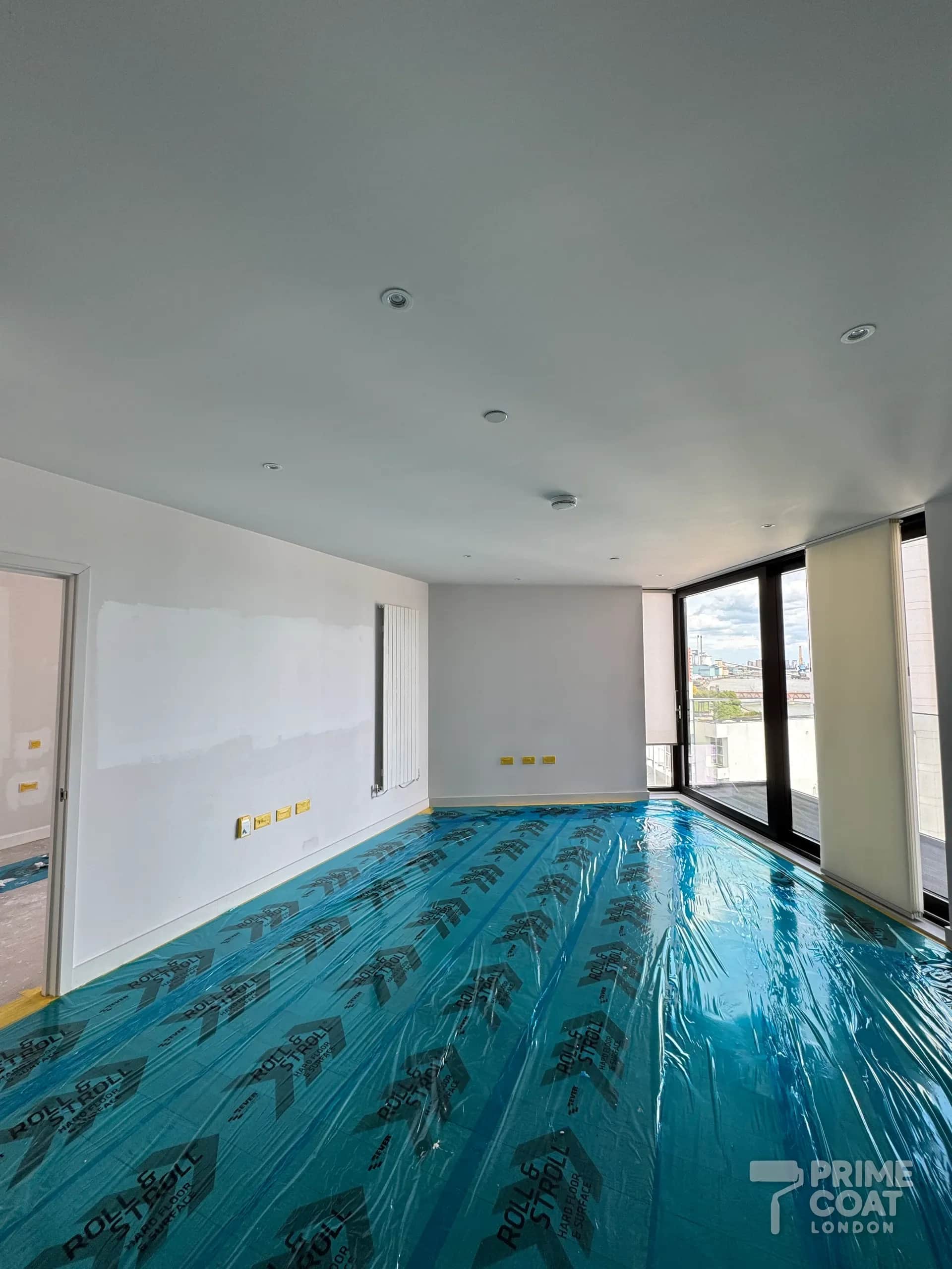 Pontoon Dock E16 new-build living room during preparation — patched walls, masked sockets and the oak floor covered in protection film