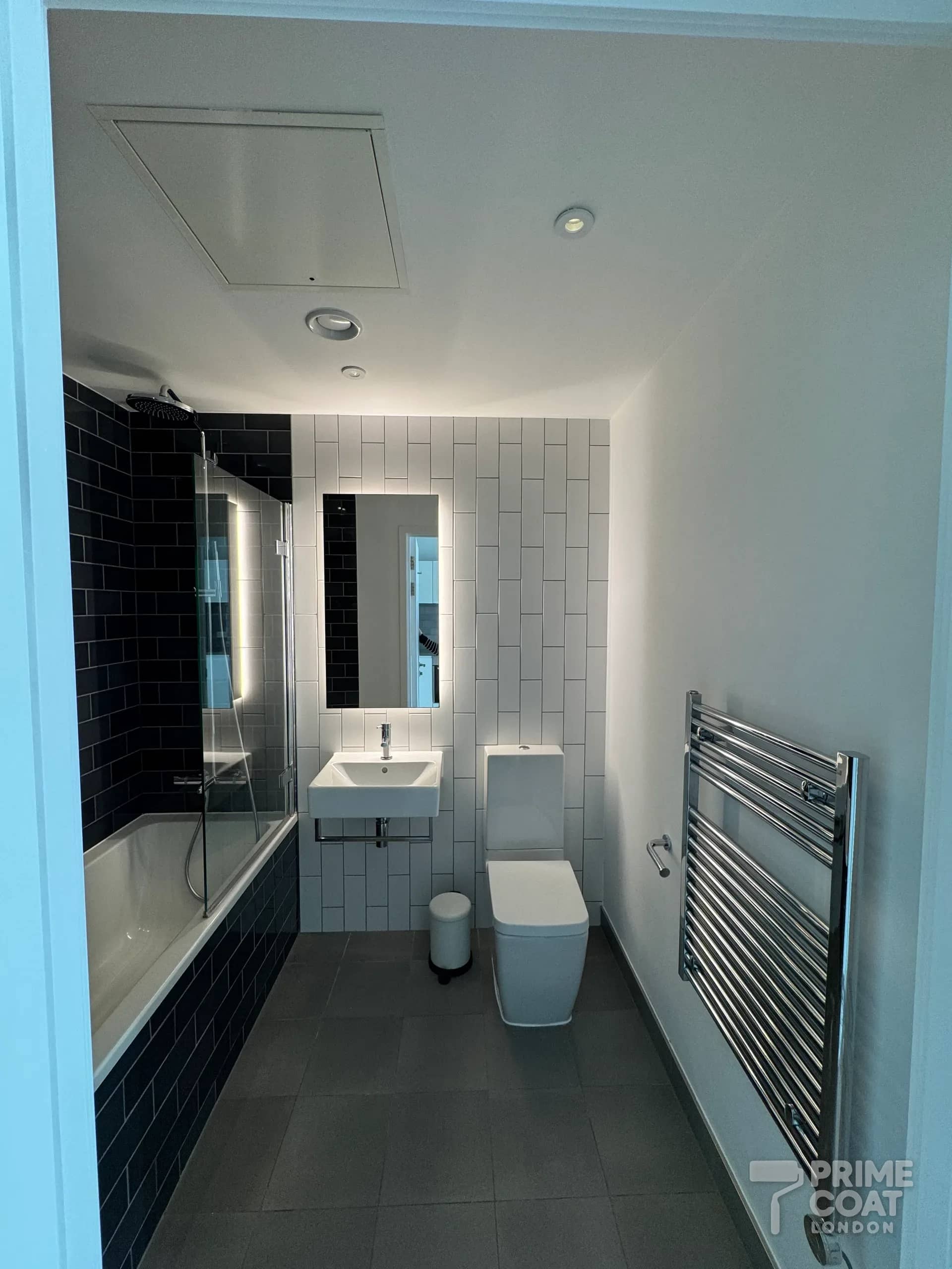 Bathroom in a Pontoon Dock E16 apartment with a freshly painted white ceiling, neatly cut in around the downlights, extractor and loft hatch, and painted walls meeting the tiling